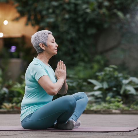Older woman in seated yoga pose with palms together.