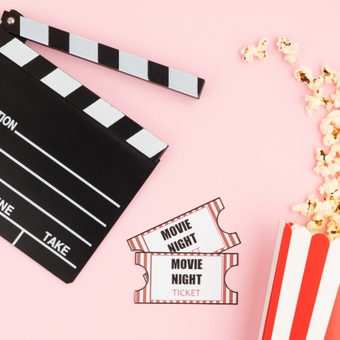 movie clapboard, tickets, and bucket of popcorn on pink background