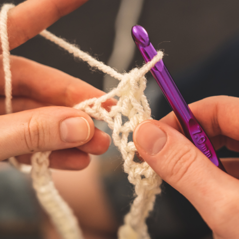 Hands with purple crochet hook and white yarn