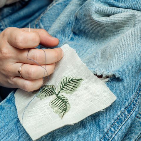 Person stitching a patch to ripped pair of jeans