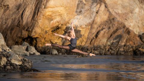 woman in black dance costume leaps on the beach