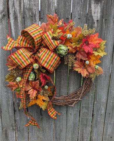 Brown wreath decorated with fall foliage and ribbon. 