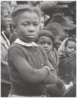 Young African-American girl with her arms crossed stares into the camera.