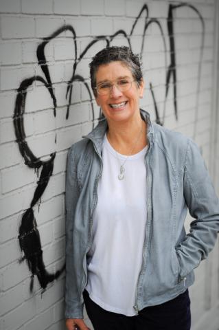 A woman stands in front of a gray wall decorated with graffiti. 
