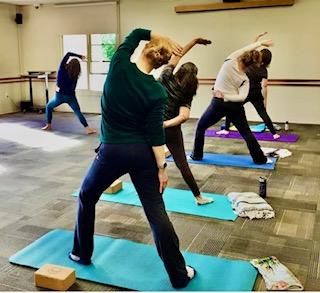 Group of women standing and stretching on blue and purple yoga mats.